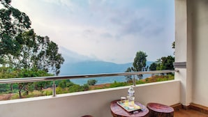 A balcony with a view of the sea and mountains, a table with a bottle, and two wooden stools. - Harmony Palace (Mahabaleshwar)