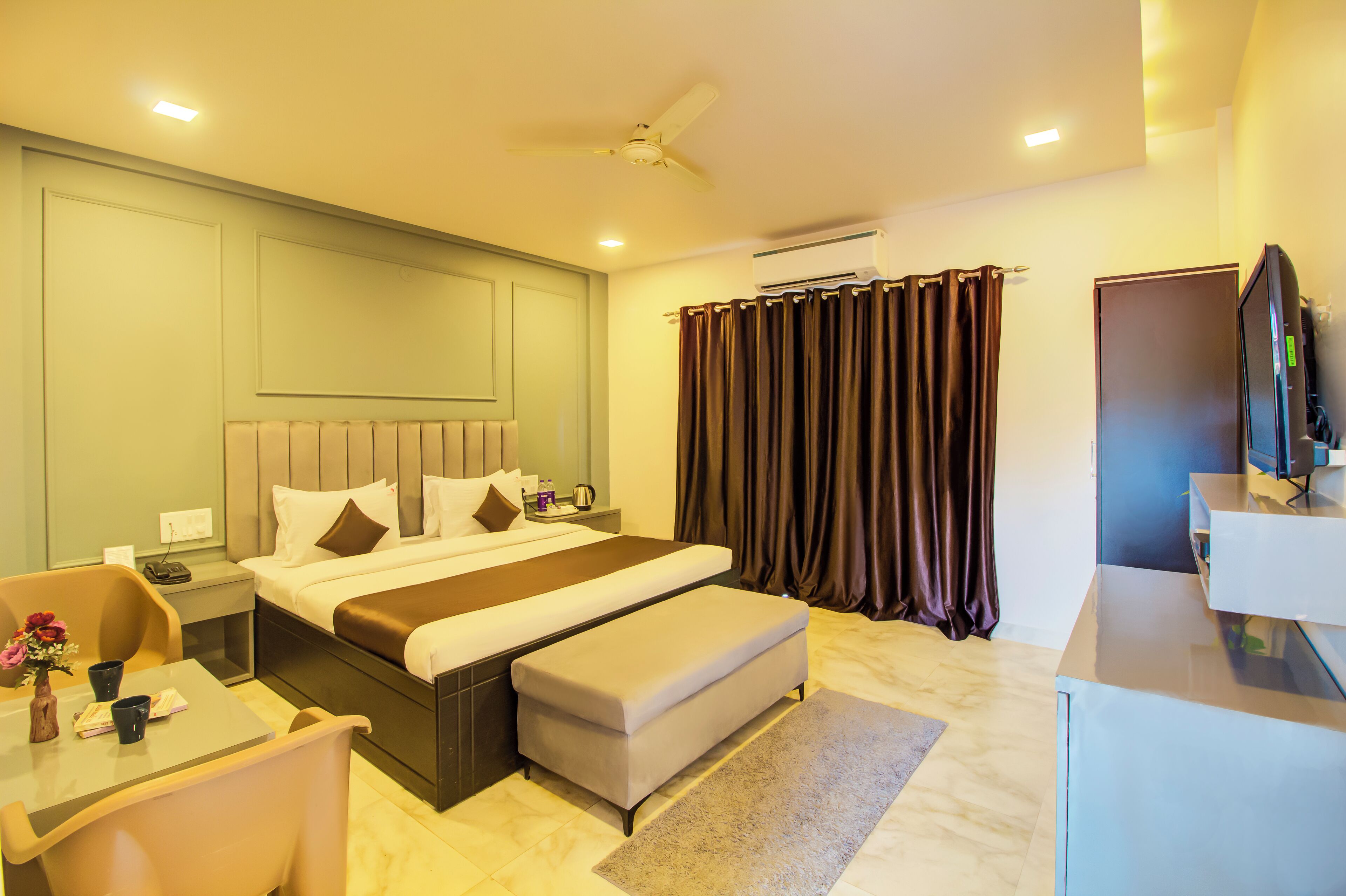 A hotel room with a bed, bedside table, chair, TV, and curtains.