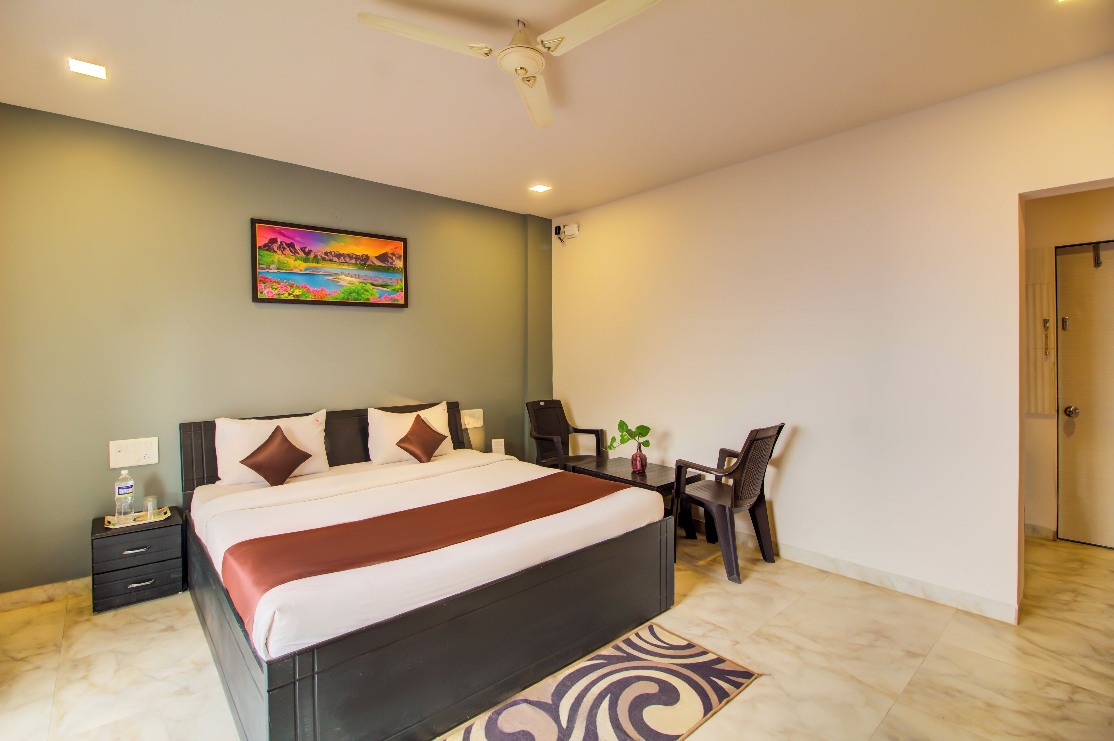 Una habitación de hotel con cama, escritorio, silla y un cuadro en la pared.