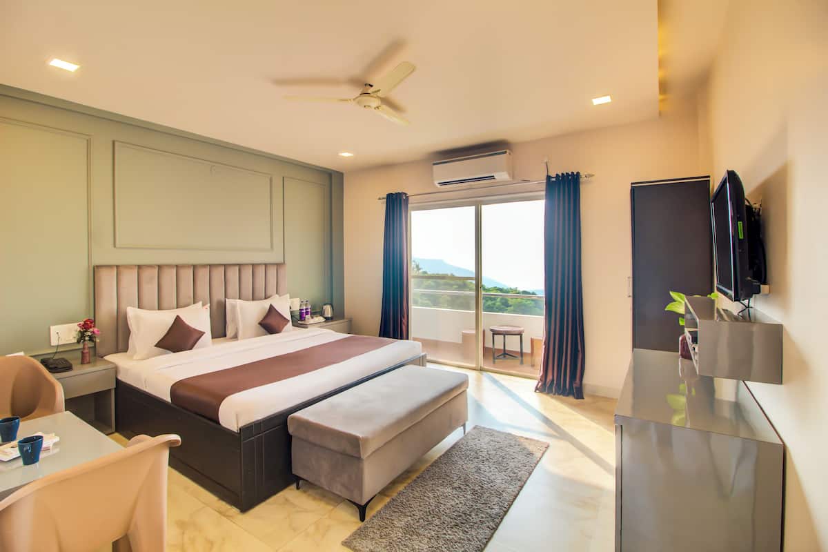A modern hotel room with a large bed, a desk, a flat-screen TV, and a balcony with a view.