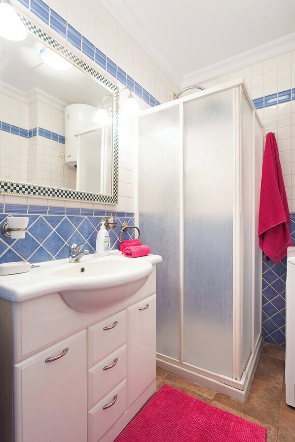 A bathroom with a white sink, a mirror, a shower enclosure, and a pink towel.