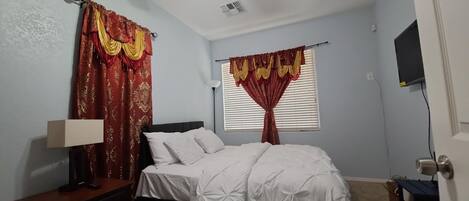 A bedroom with a bed, a nightstand, a lamp, and curtains.