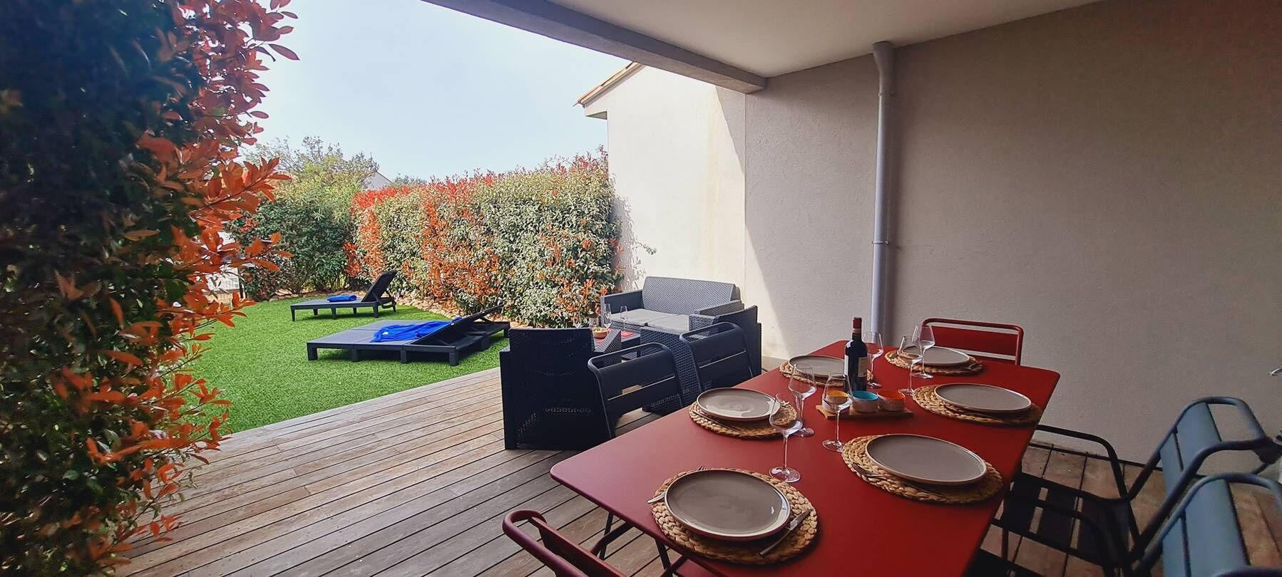 Eine Terrasse im Freien mit einem roten Esstisch, umgeben von Stühlen und einem Grill.