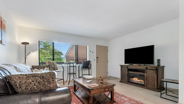 A modern living room with a leather sofa, a coffee table, a fireplace, a TV, and a large window with blinds. - Sedona Eve

 (Sedona)