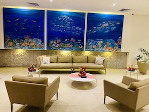 A modern living room with a beige sofa, two armchairs, and a coffee table. There are three large paintings of underwater scenes on the wall.