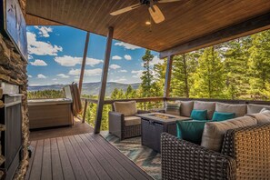 A covered outdoor deck with wicker furniture, a stone wall, and a hot tub. - Mountain Vista Villa (Angel Fire)