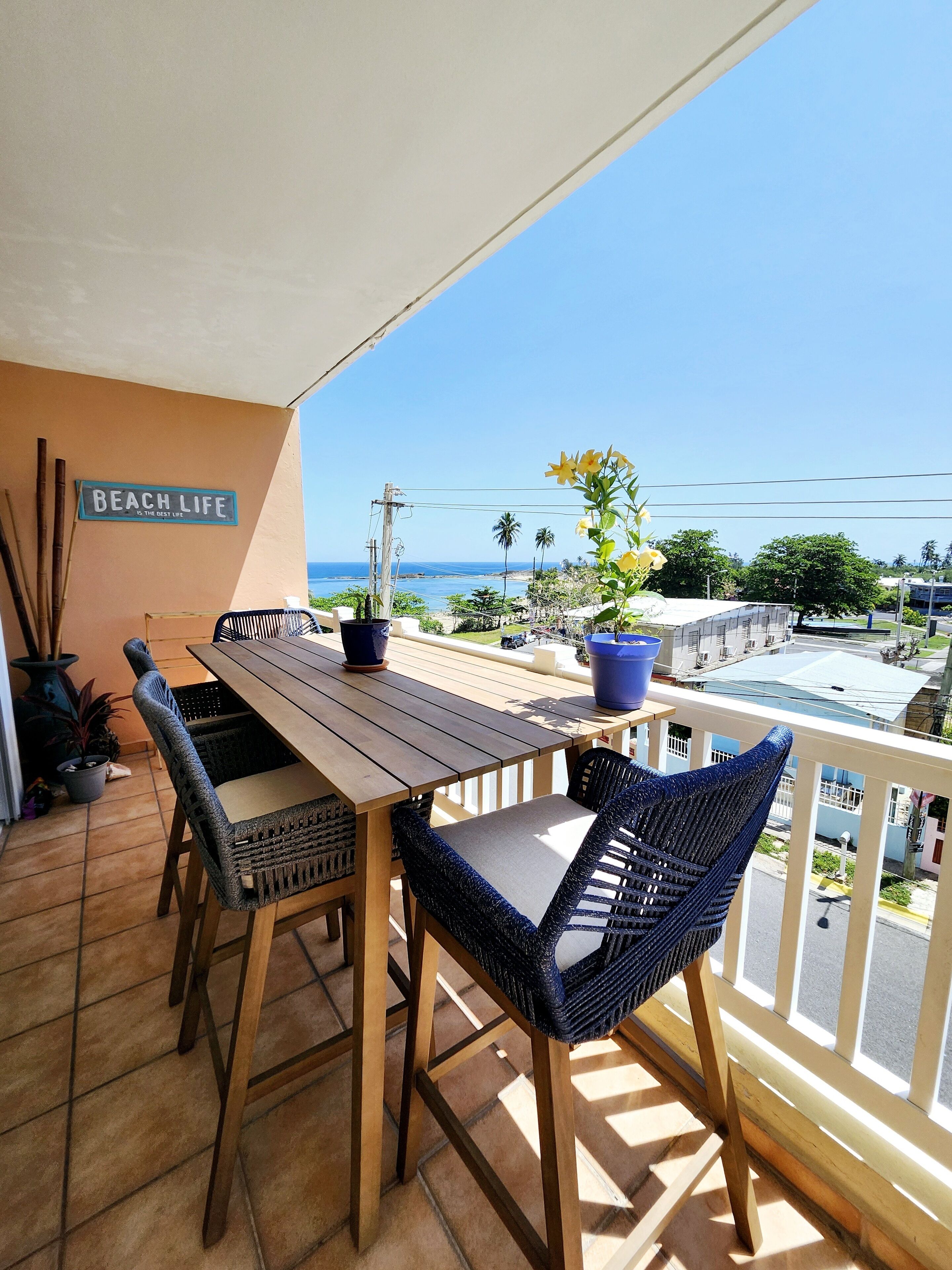 A wooden table and chairs on a balcony with a view of the sea.