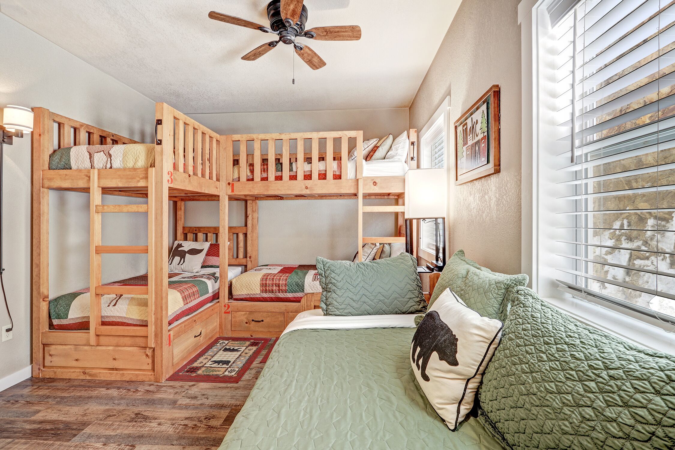 A bunk bed room with a ceiling fan, a window with blinds, and a framed picture on the wall.
