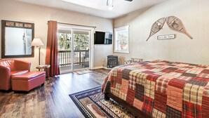 A bedroom with a bed, a ceiling fan, a TV, a red chair, and a sliding glass door leading to a balcony. - Parkview at Red River (Red River)