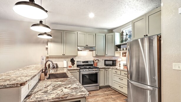 A kitchen with light green cabinets, stainless steel appliances, and a granite countertop. - Parkview at Red River (Red River)