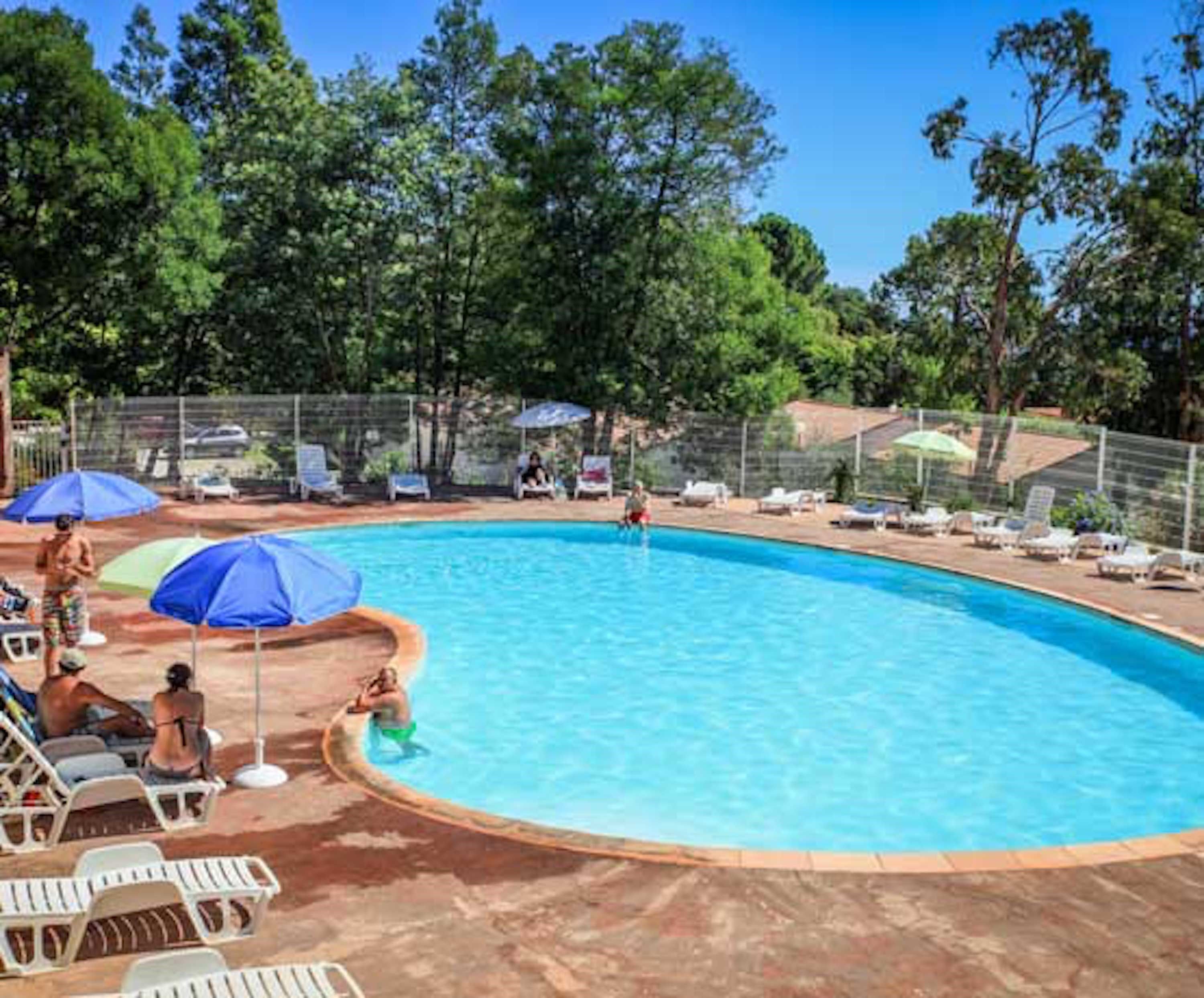Une piscine entourée d’arbres, avec des chaises longues et des parasols.