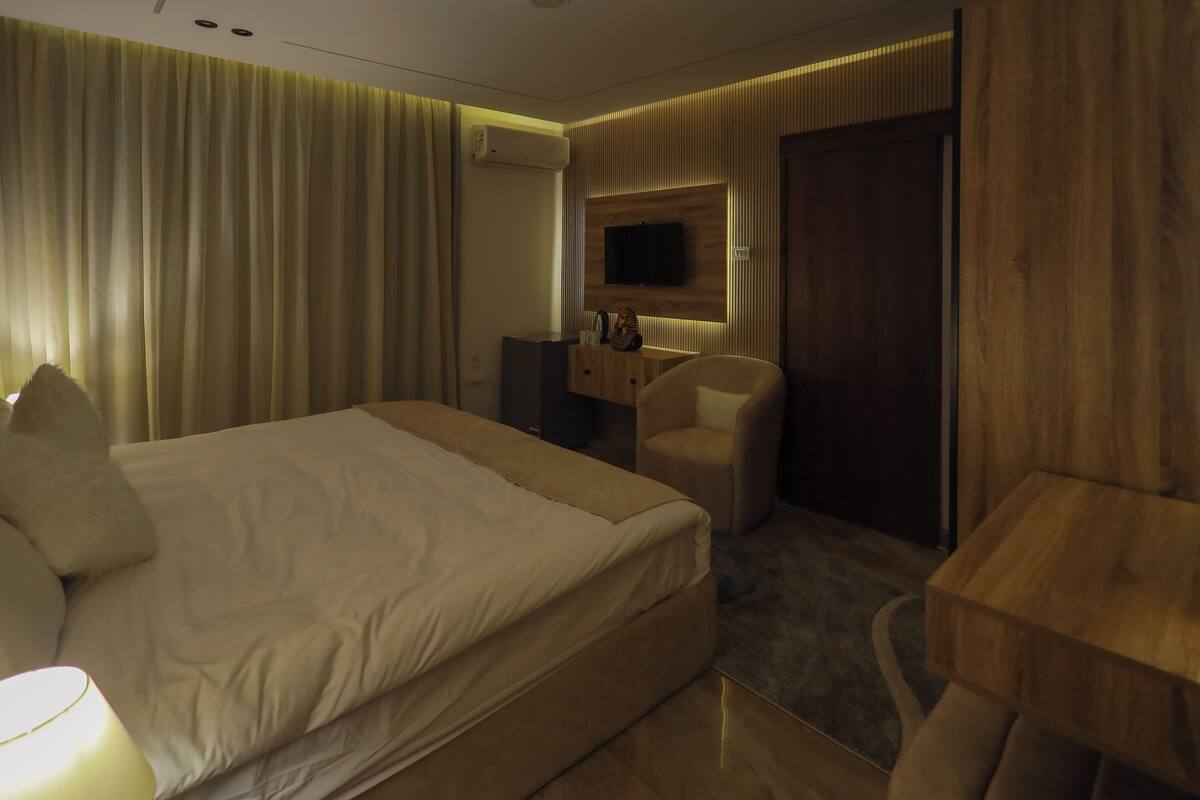 A hotel room with a large bed, a desk, a chair, a TV mounted on the wall, and a wooden panel design.