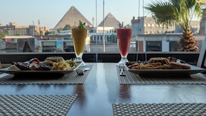 Une table avec deux assiettes de nourriture et deux boissons, avec une vue sur les pyramides en arrière-plan.