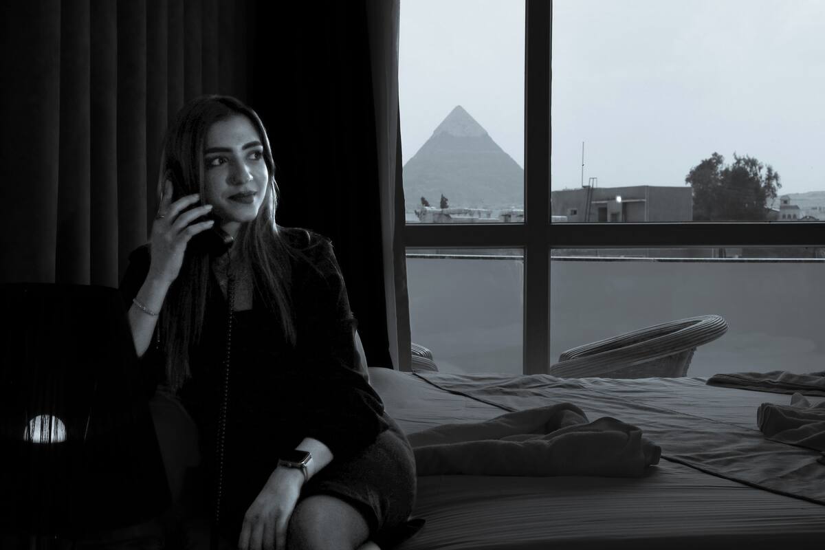 A person sitting on a bed in a room with a view of a pyramid through a window.