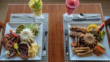 Two square plates of food with cutlery and glasses on a table.