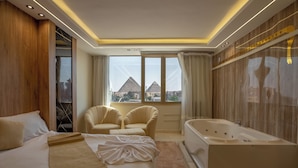 Une chambre d’hôtel moderne dotée d’un grand lit, de deux fauteuils, d’une baignoire et offrant une vue sur les pyramides.
