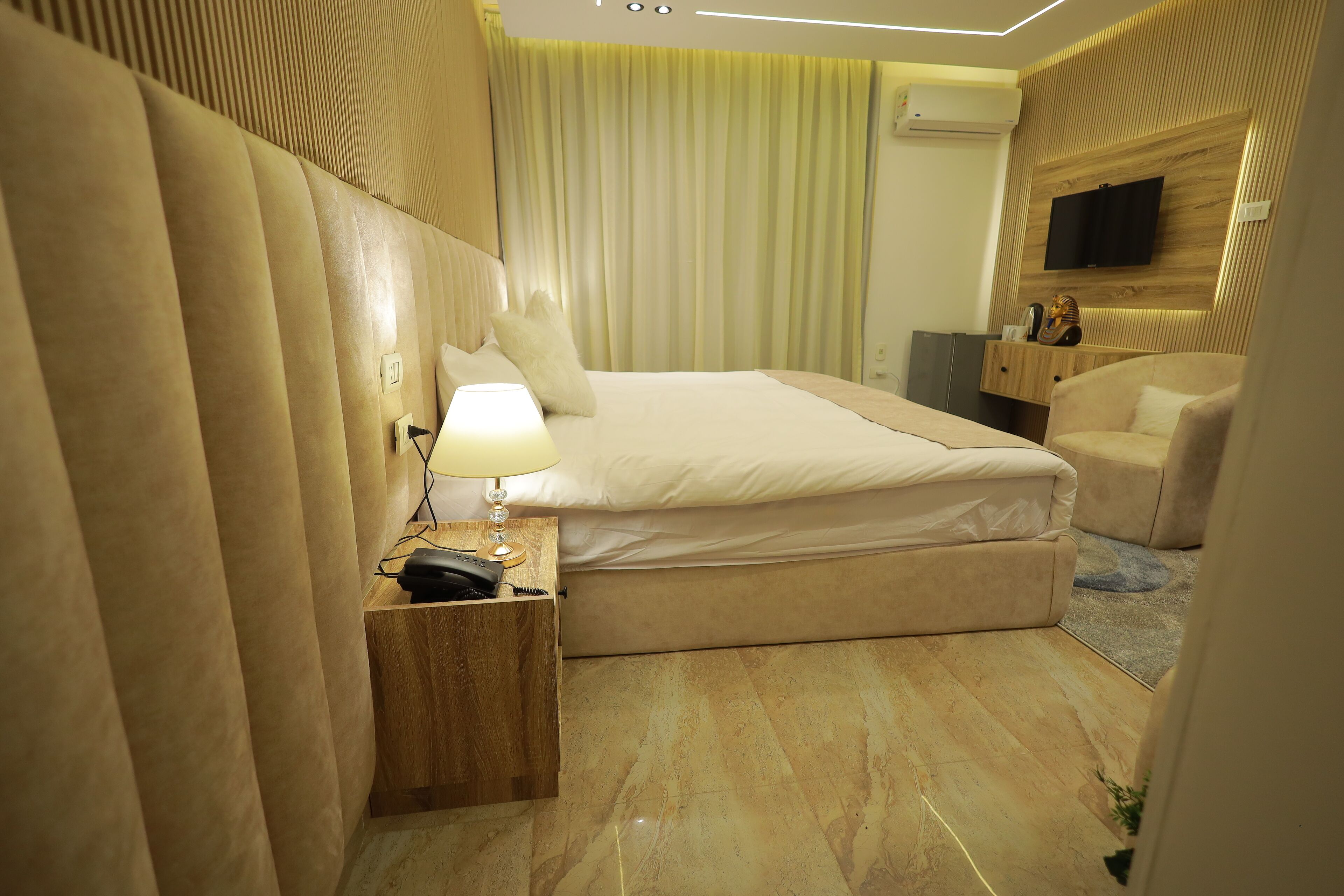 Ein Hotelzimmer mit einem großen Bett, einem Nachttisch mit Lampe, einem an der Wand montierten Fernseher und einer Sitzecke mit einem Sessel.