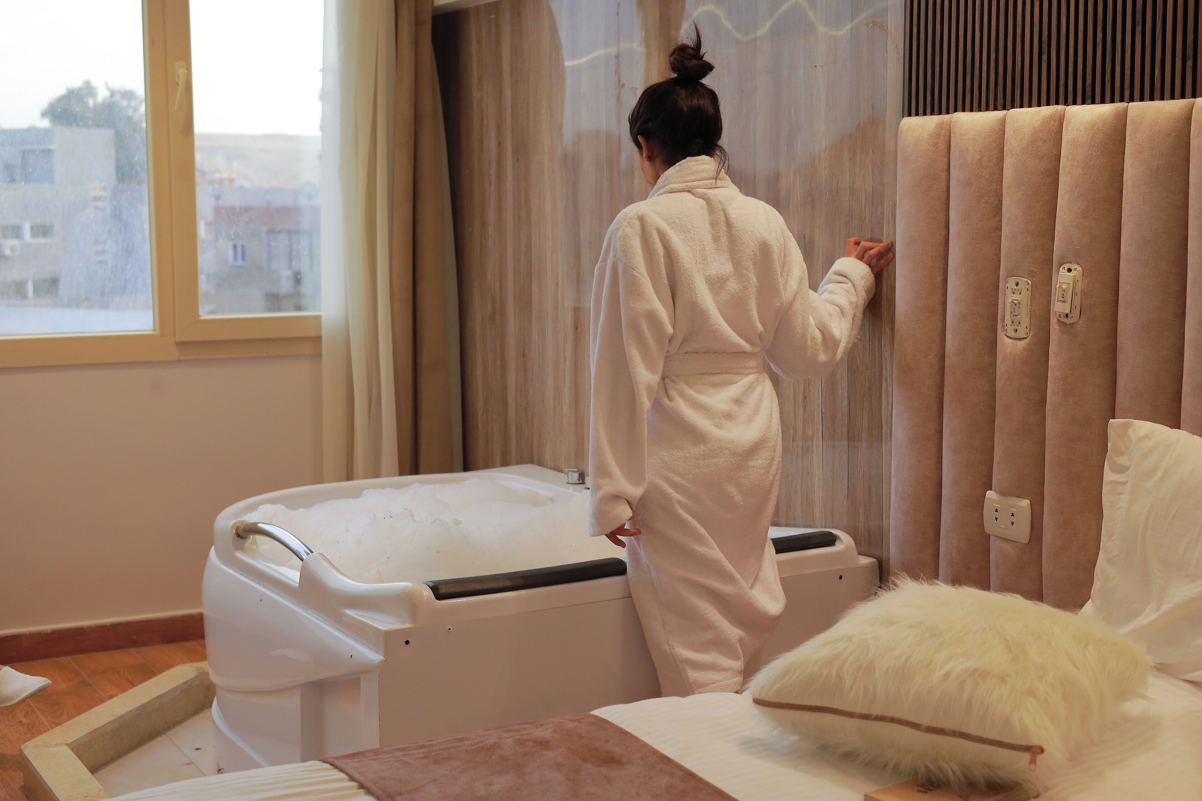 A room with a bed, a window, and a white bathtub.
