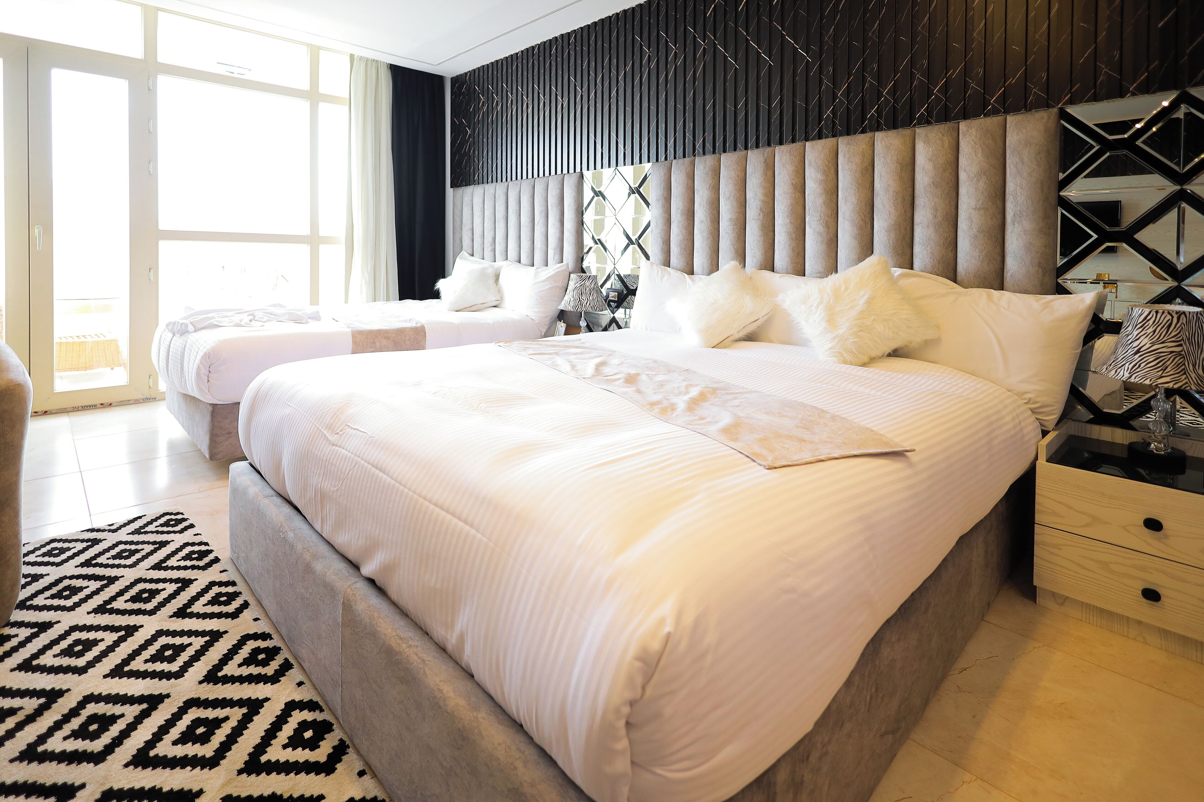 Quarto de hotel moderno com uma cama grande, um sofá e um tapete estampado.
