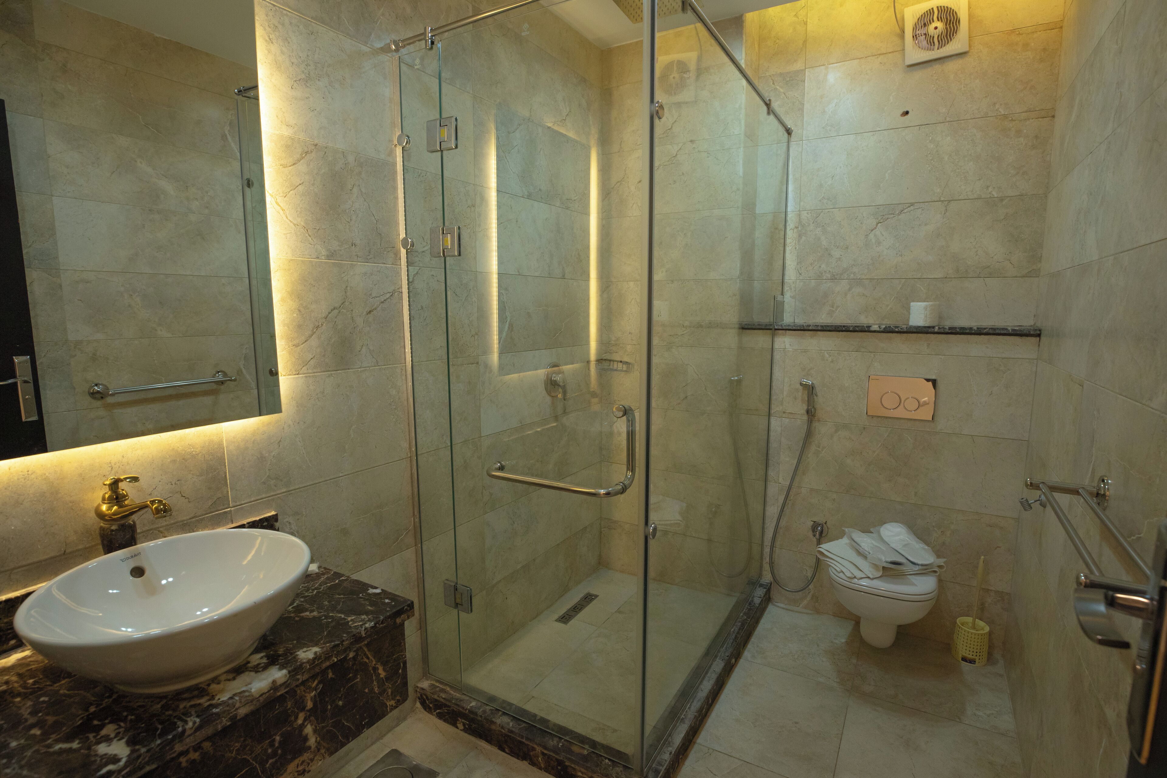 A bathroom with a glass-enclosed shower, a marble sink, and a toilet.