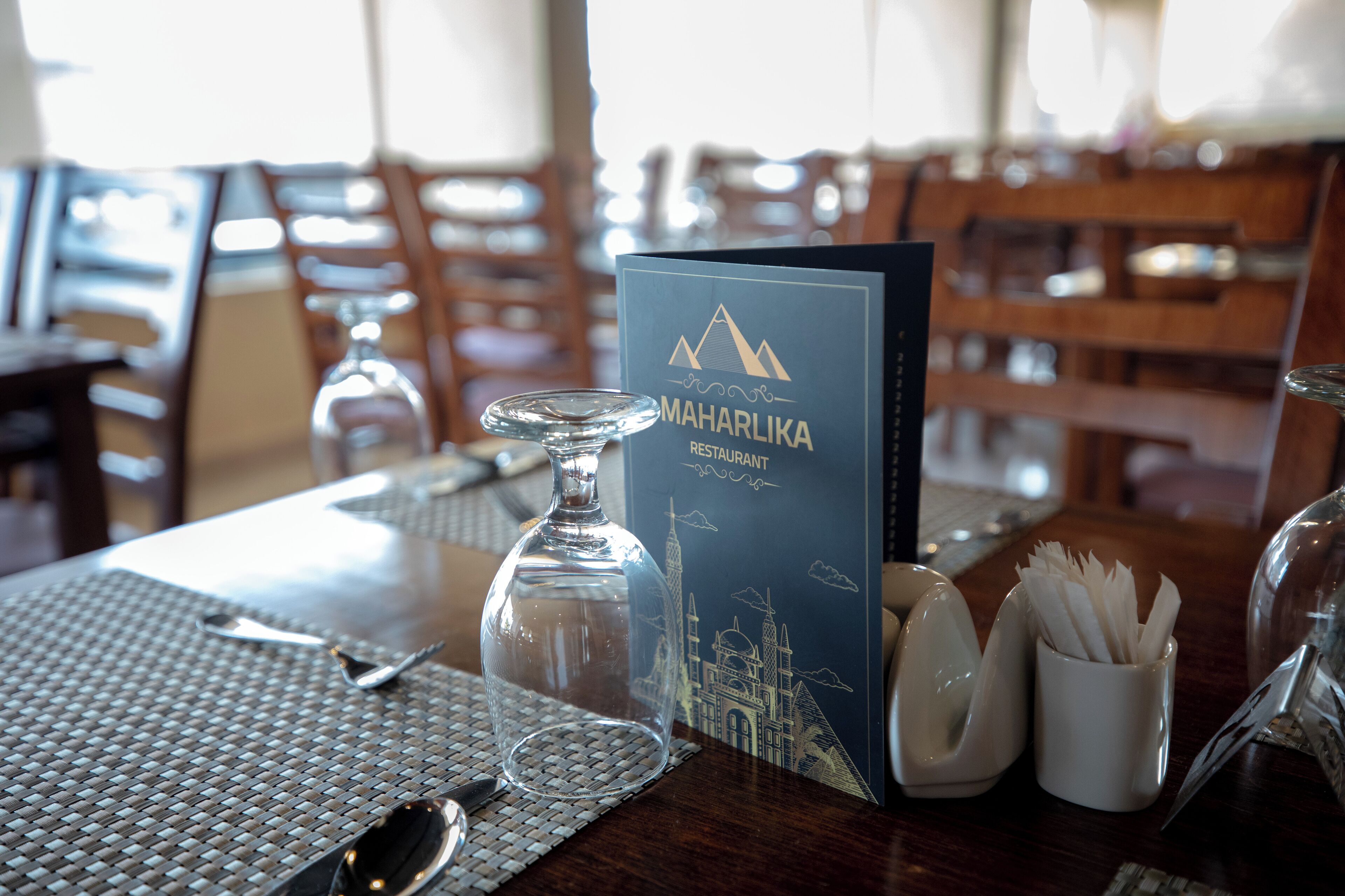 Un ambiente de restaurante con una mesa preparada para comer, que incluye un menú, una jarra de cristal, cubiertos y un portavelas.