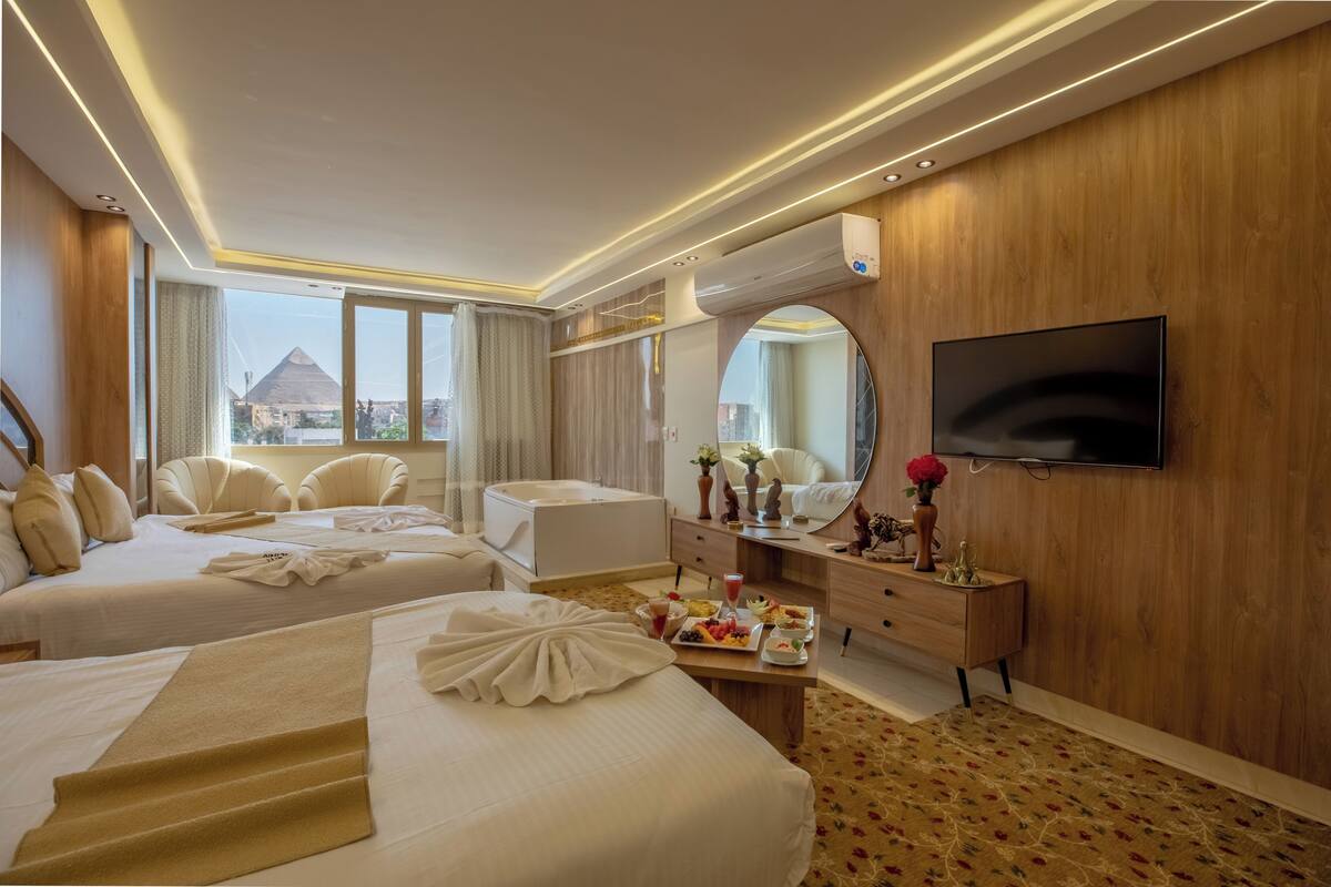 A hotel room with two beds, a sitting area, a vanity with a mirror, and a television mounted on the wall.