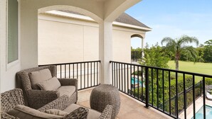 Een balkon met rieten meubilair, een zwembad en uitzicht op een golfbaan.