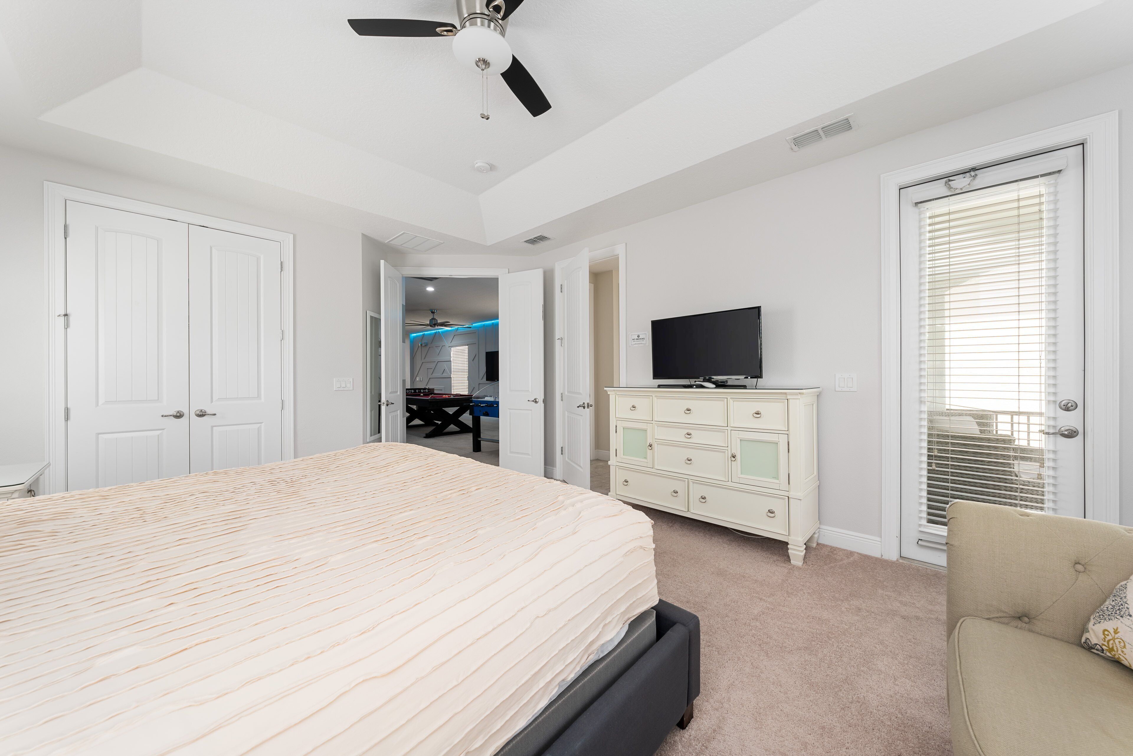 A bedroom with a bed, a dresser, a television, and a ceiling fan.