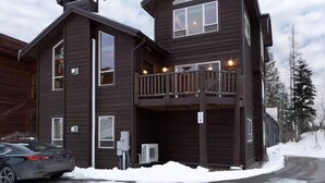 Eine zweistöckige Holzhütte mit Balkon, ein Auto davor und Schnee auf dem Boden.