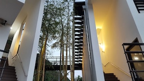 Un edificio moderno con una escalera central flanqueada por barandales de cristal y una estructura de bambú.