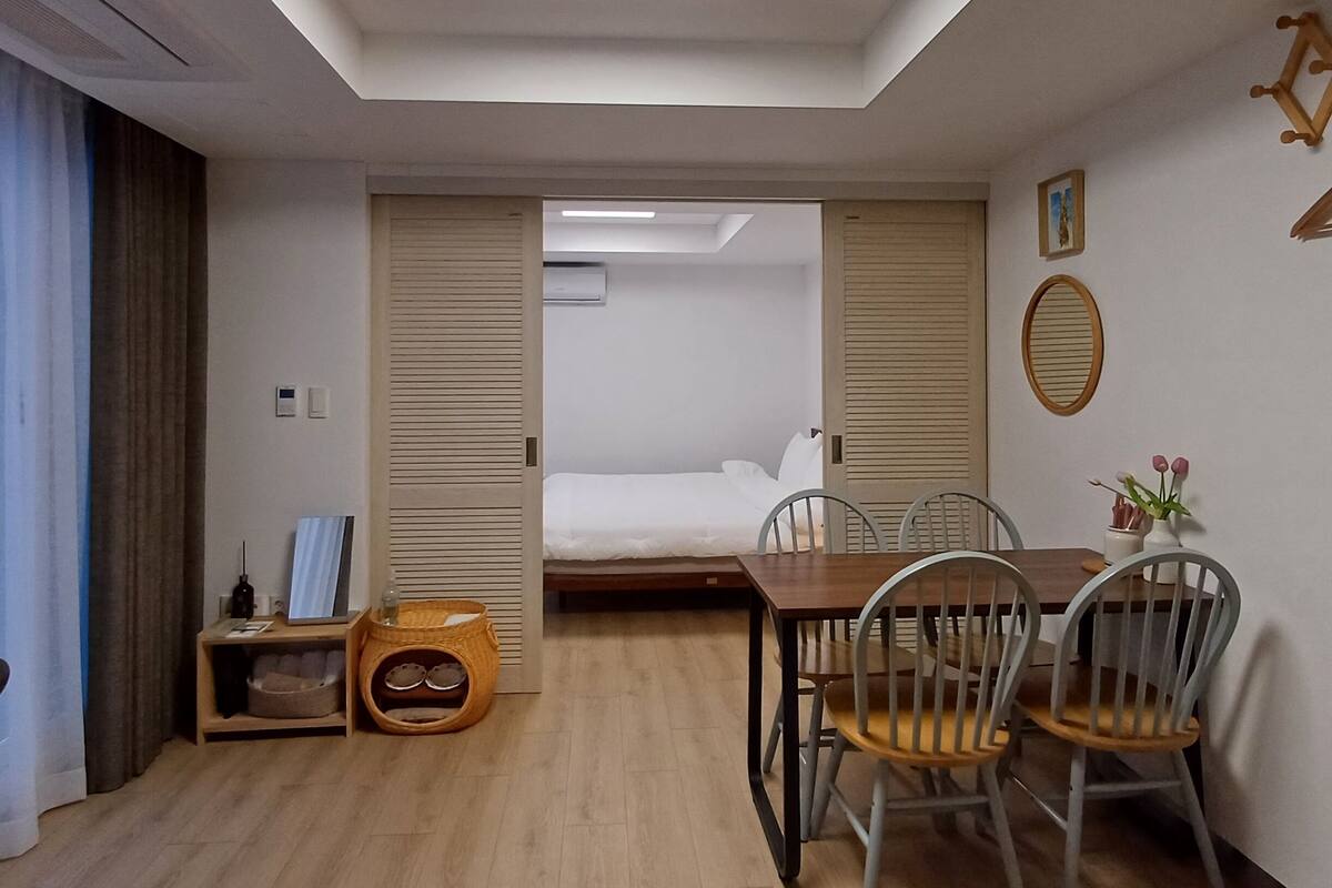 A modern hotel room with a skylight, a bed, a dining area with chairs, a small table, and a pet bed.