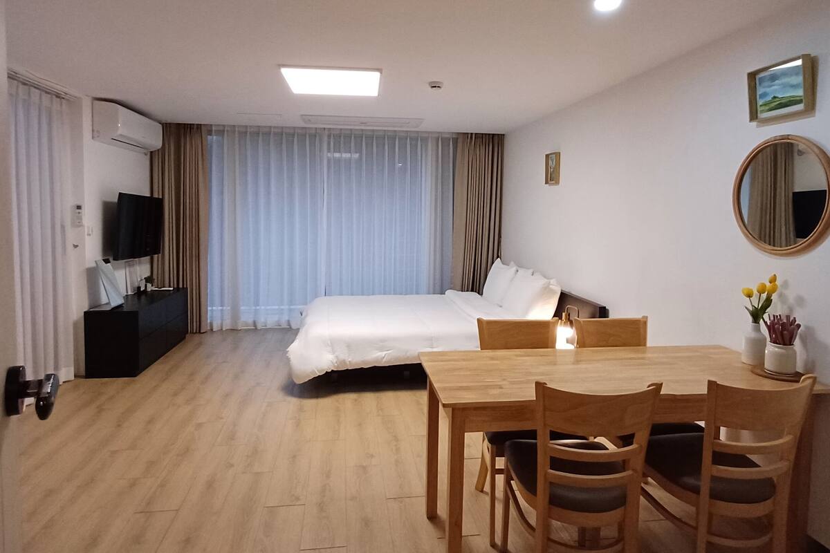A hotel room with a bed, a desk, a chair, a TV, and a mirror.