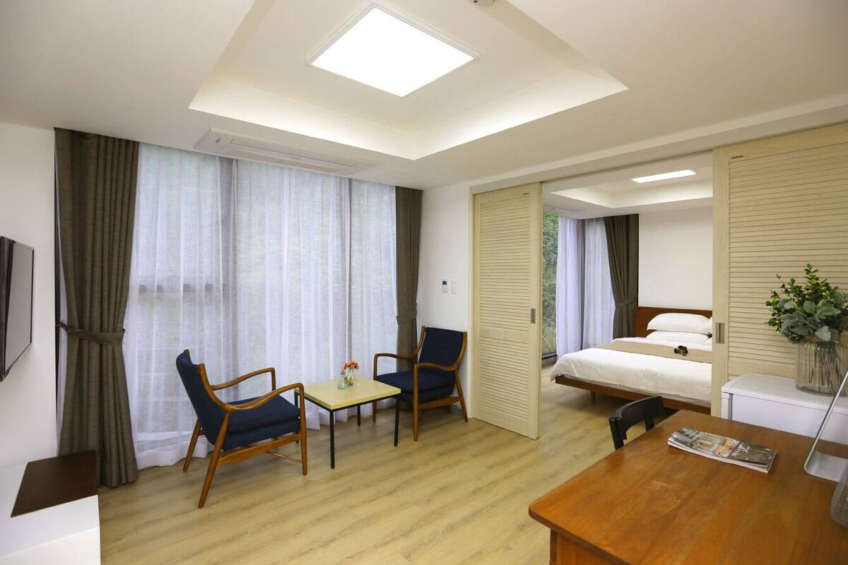 A hotel room with a bed, a desk, two chairs, a TV, and a window with curtains.