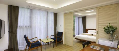 A hotel room with a bed, a desk, two chairs, a TV, and a window with curtains.