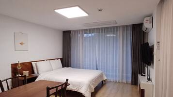 Habitación de hotel con una cama, un escritorio con silla, televisión y ventana con cortinas.