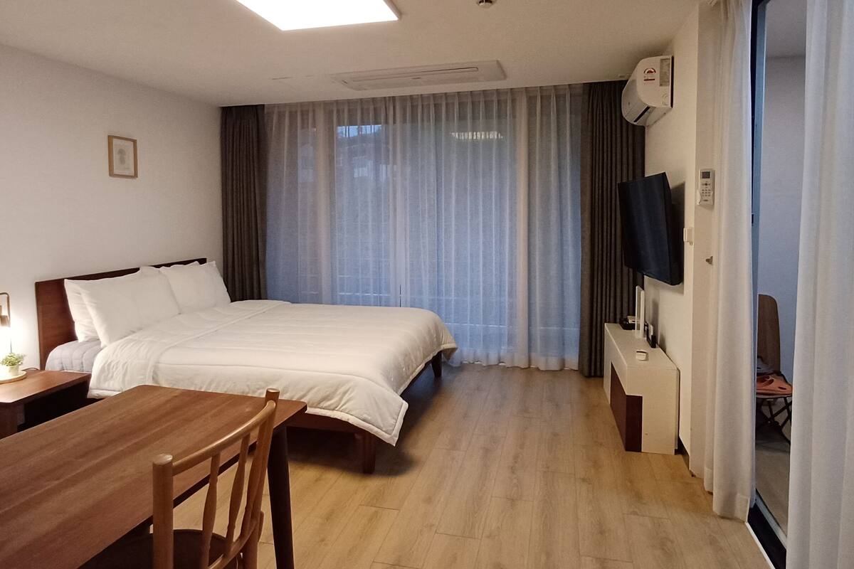 A hotel room with a bed, a desk, a chair, a TV, and a window with curtains.