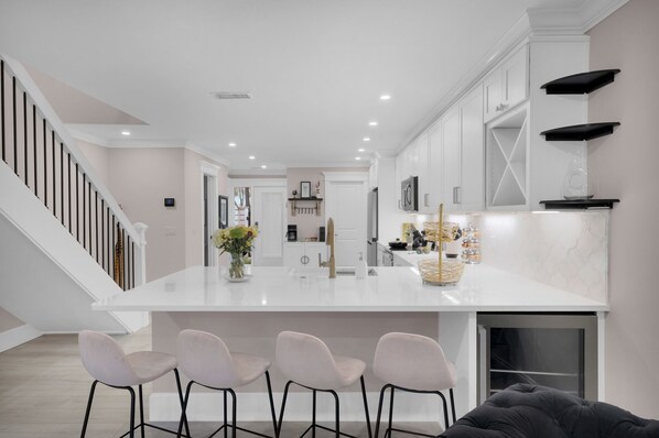 Una cocina moderna con armarios blancos, una isla central con taburetes y una escalera a la izquierda.