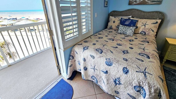 Een slaapkamer met uitzicht op het strand, een balkon met een hekwerk en een bed met een decoratieve spreideken.