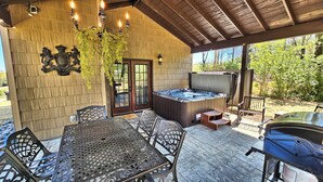 Une terrasse extérieure équipée d’un jacuzzi, d’un barbecue et d’un coin repas avec des chaises et une table en métal.