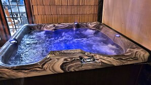 Un bain à remous avec un revêtement extérieur imitant le marbre, un panneau de commande et un mur en bois en arrière-plan.