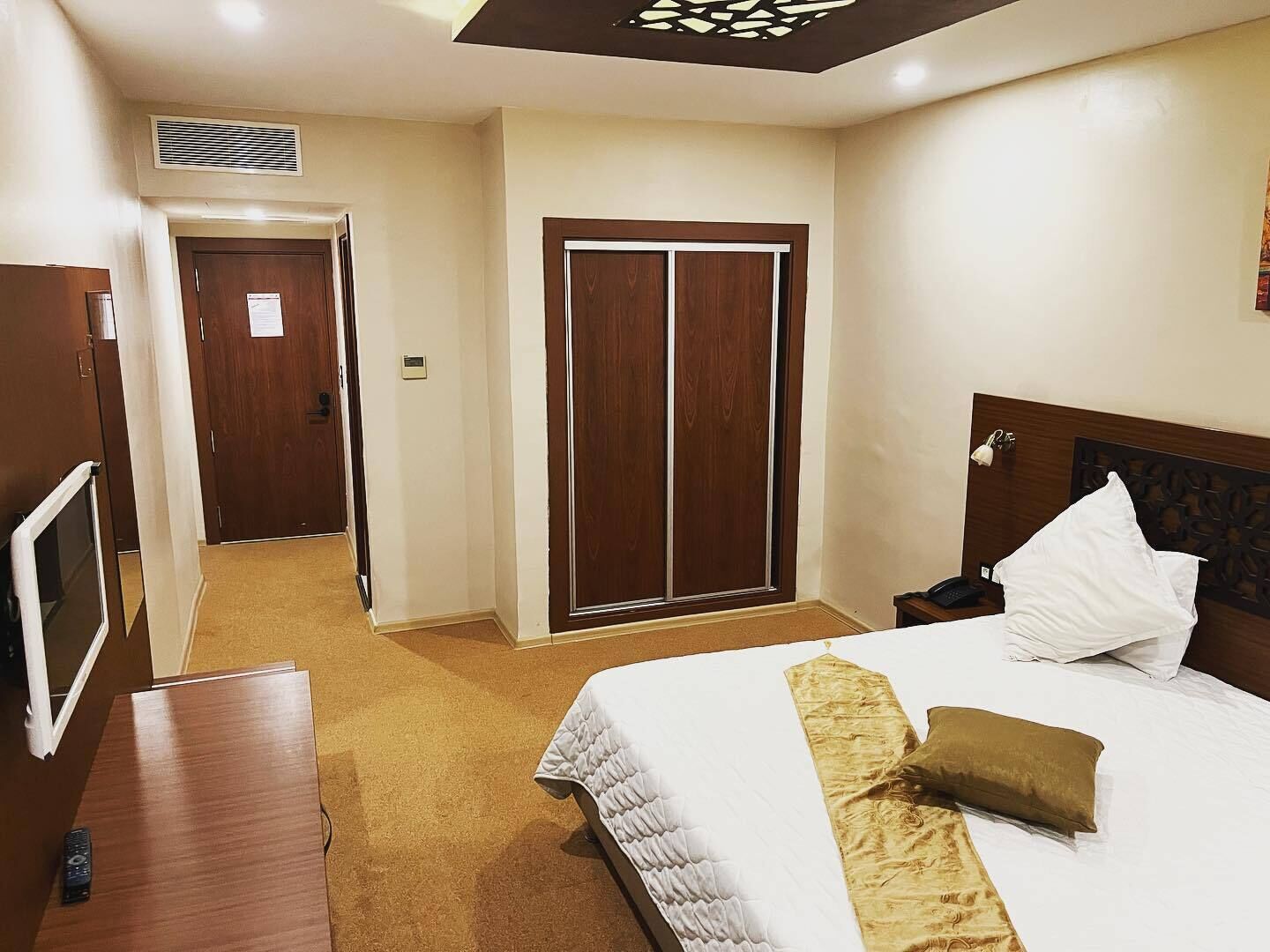 A hotel room with a bed, a bedside table, a TV, a wardrobe, and a door.