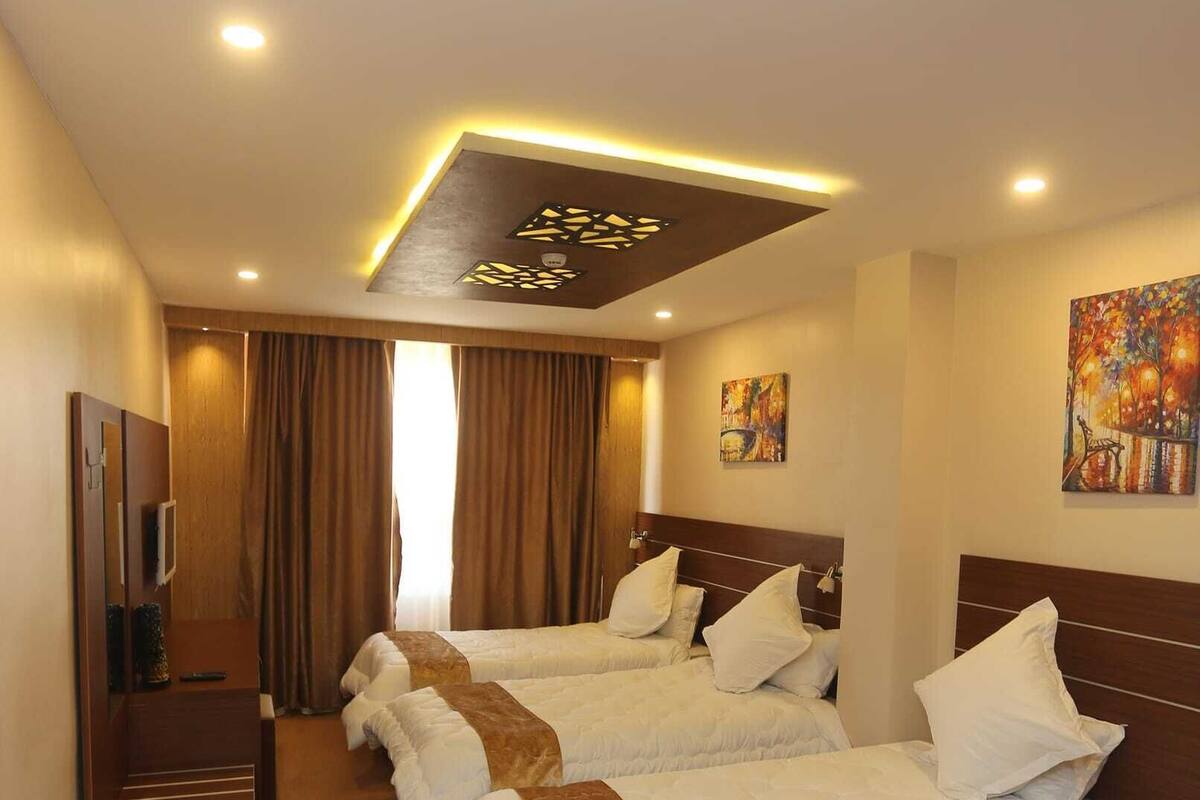 A hotel room with three beds, a TV, and a ceiling light fixture.