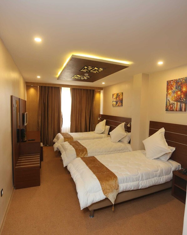 A hotel room with three beds, a TV, and a ceiling light fixture.