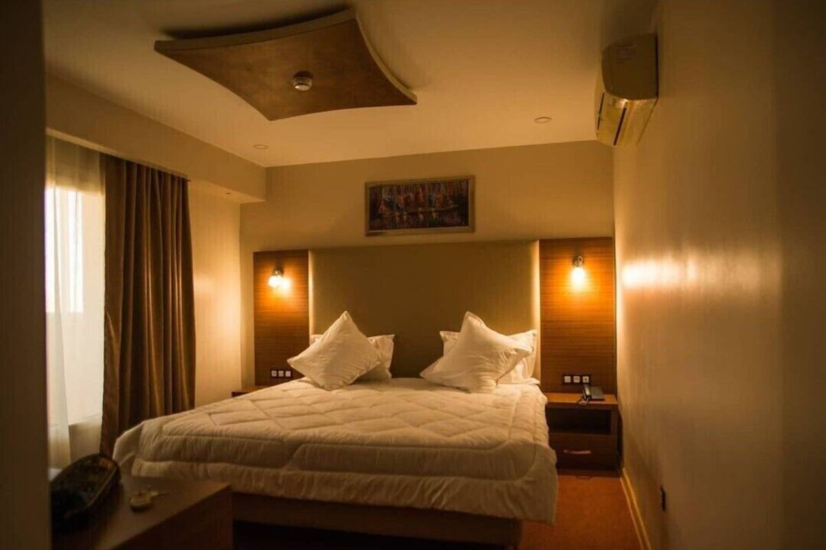 A hotel room with a large bed, two bedside tables, a ceiling light fixture, and a painting on the wall.