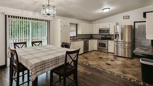 A modern kitchen with white cabinets, stainless steel appliances, and a dining area with a table and chairs. - Serene Family Home: Sleeps 16! (Wyoming)