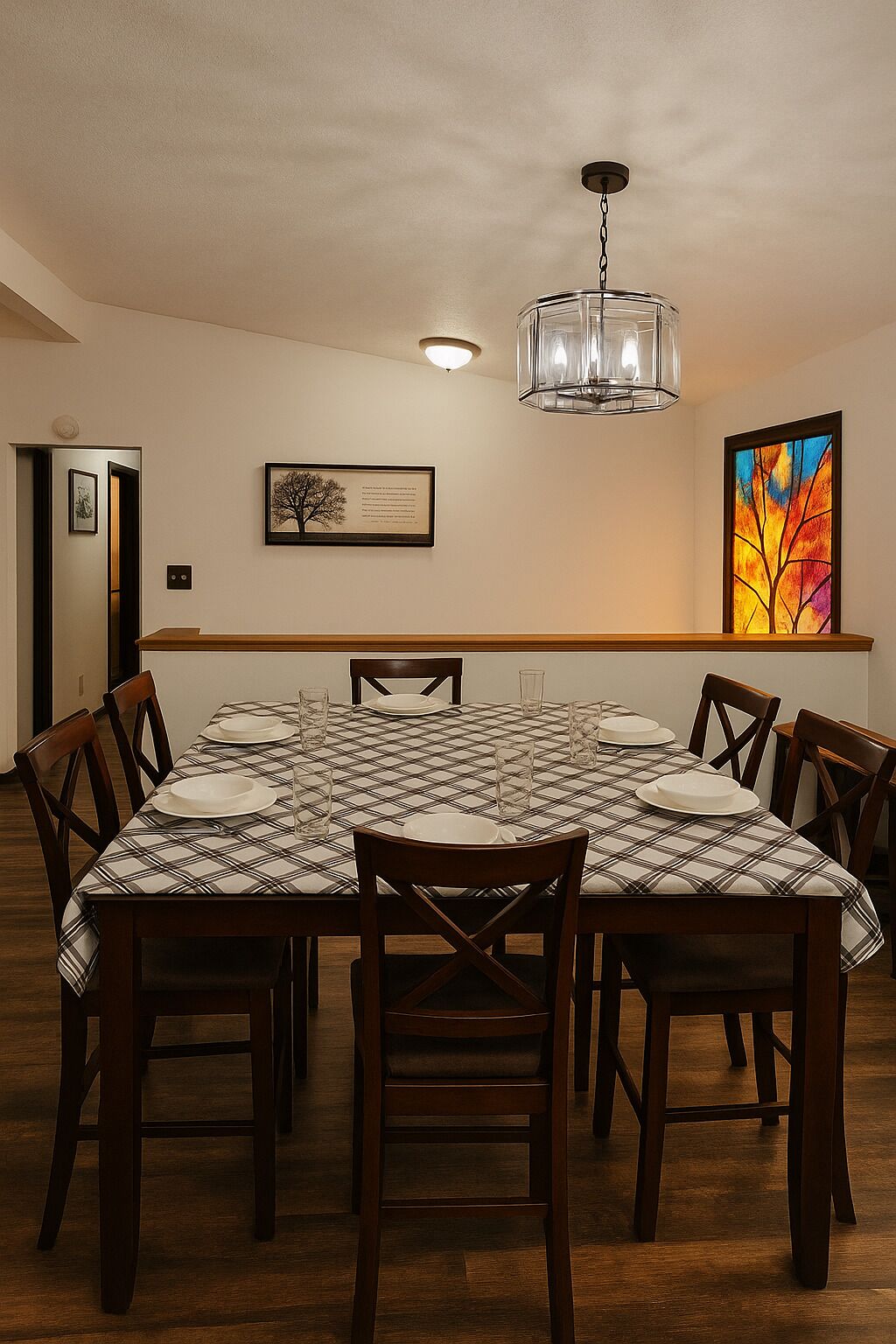 Une salle à manger avec une nappe à carreaux, des chaises en bois, un lustre et un tableau encadré au mur.