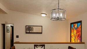 A dining room with a checkered tablecloth, wooden chairs, a chandelier, and a framed picture on the wall. - Serene Family Home: Sleeps 16! (Wyoming)