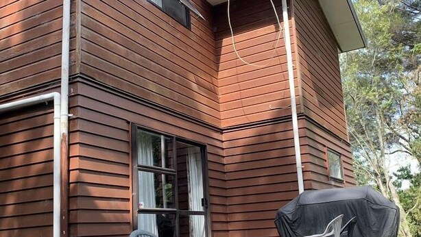 A two-story wooden house with a covered deck and a chair. - Bush paradise  (Auckland)