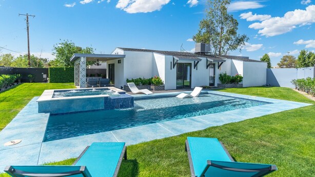 Ein modernes Haus mit Schwimmbad, Sitzgelegenheiten im Freien und einem gepflegten Rasen.