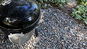 Un barbecue doté d’un couvercle noir réfléchissant, entouré d’un chemin de gravier et de verdure.
